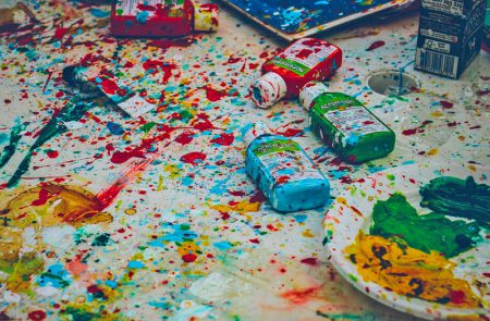 Bunte Farbkleckse und Farbtuben auf weißem Boden verteilt, kreatives Chaos beim Malen